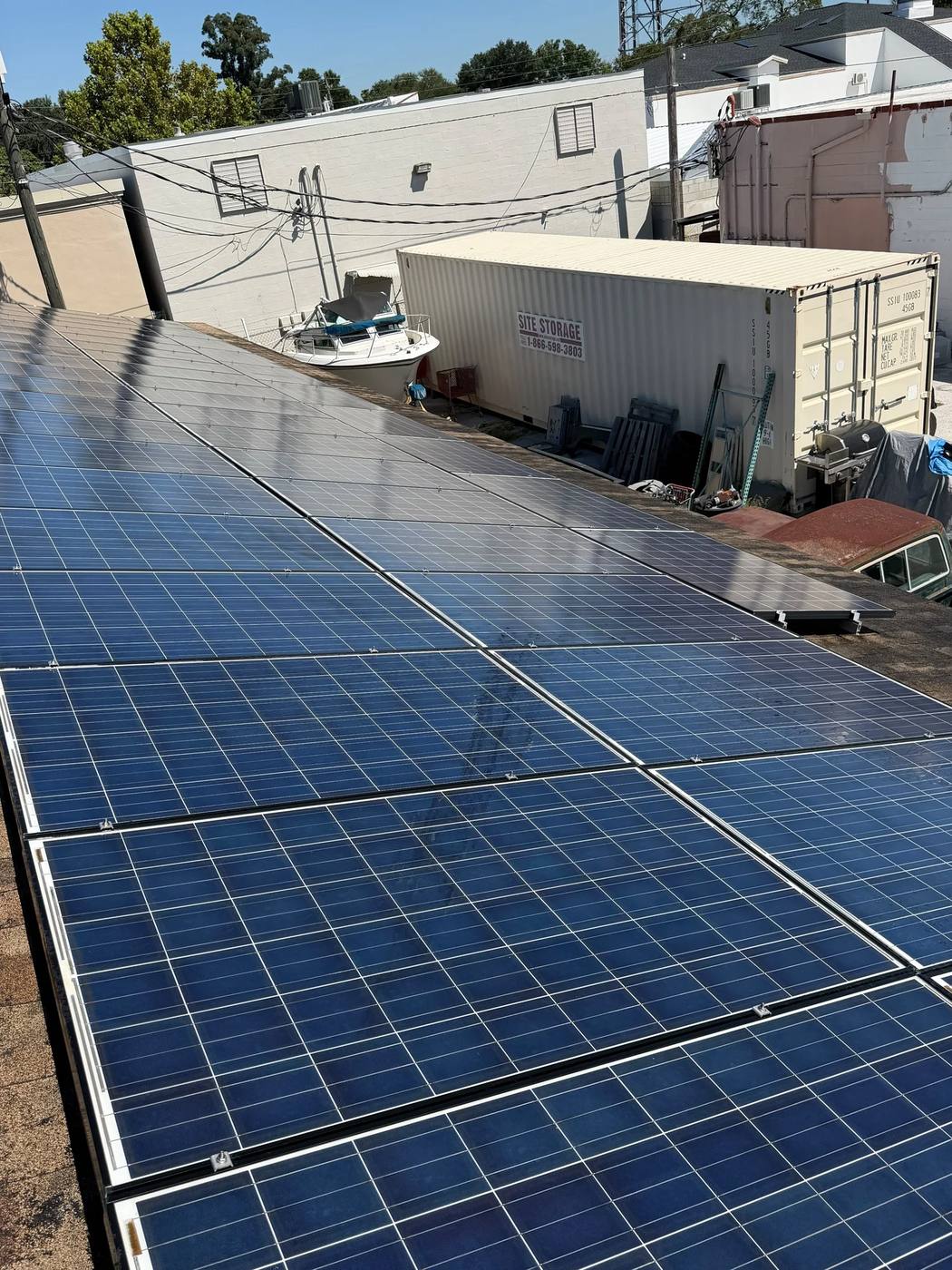 Rows of blue solar panels on a low-slope roof beside commercial buildings