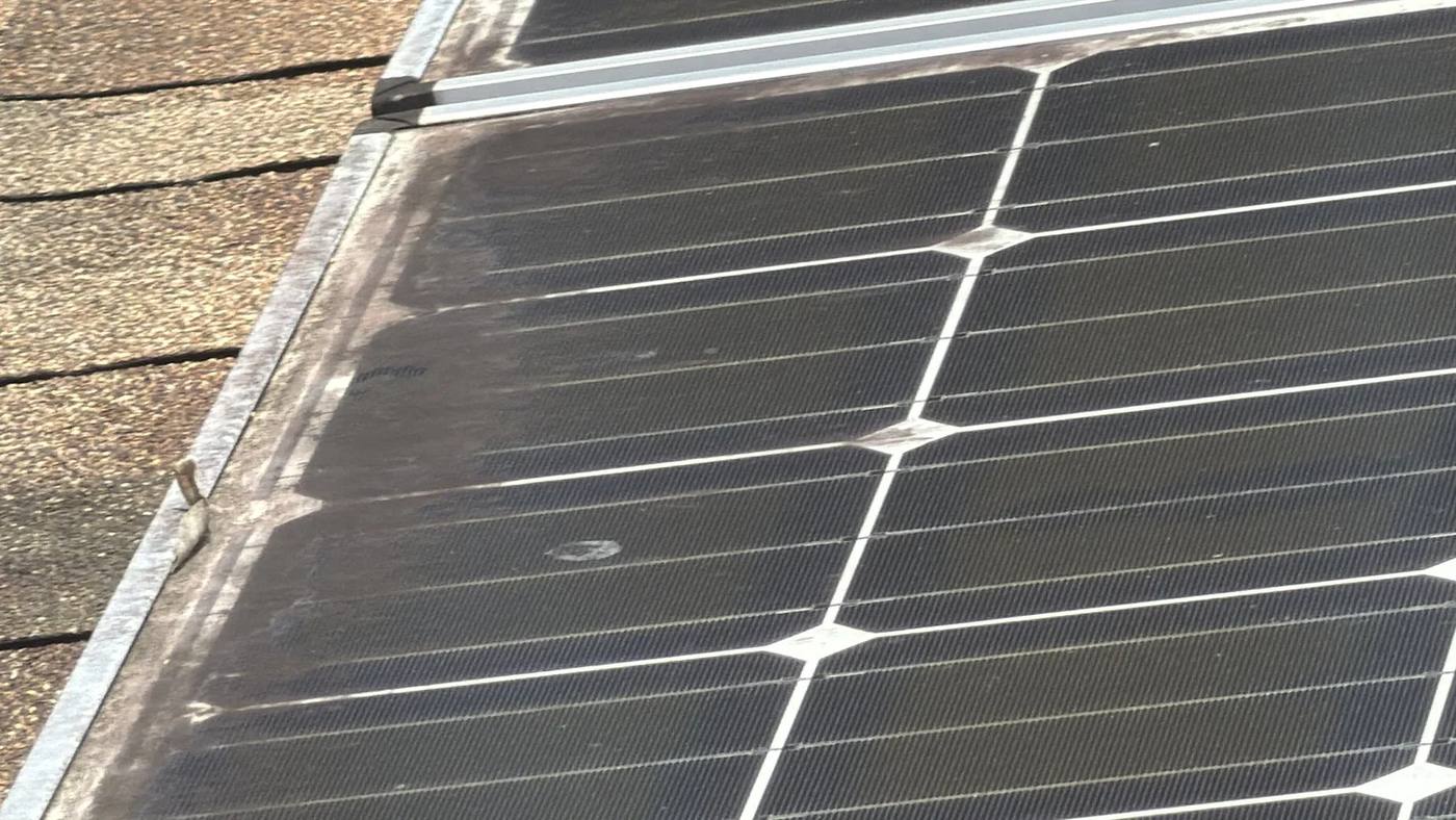 Solar panel with dirt and debris caked along its lower edge on a shingle roof