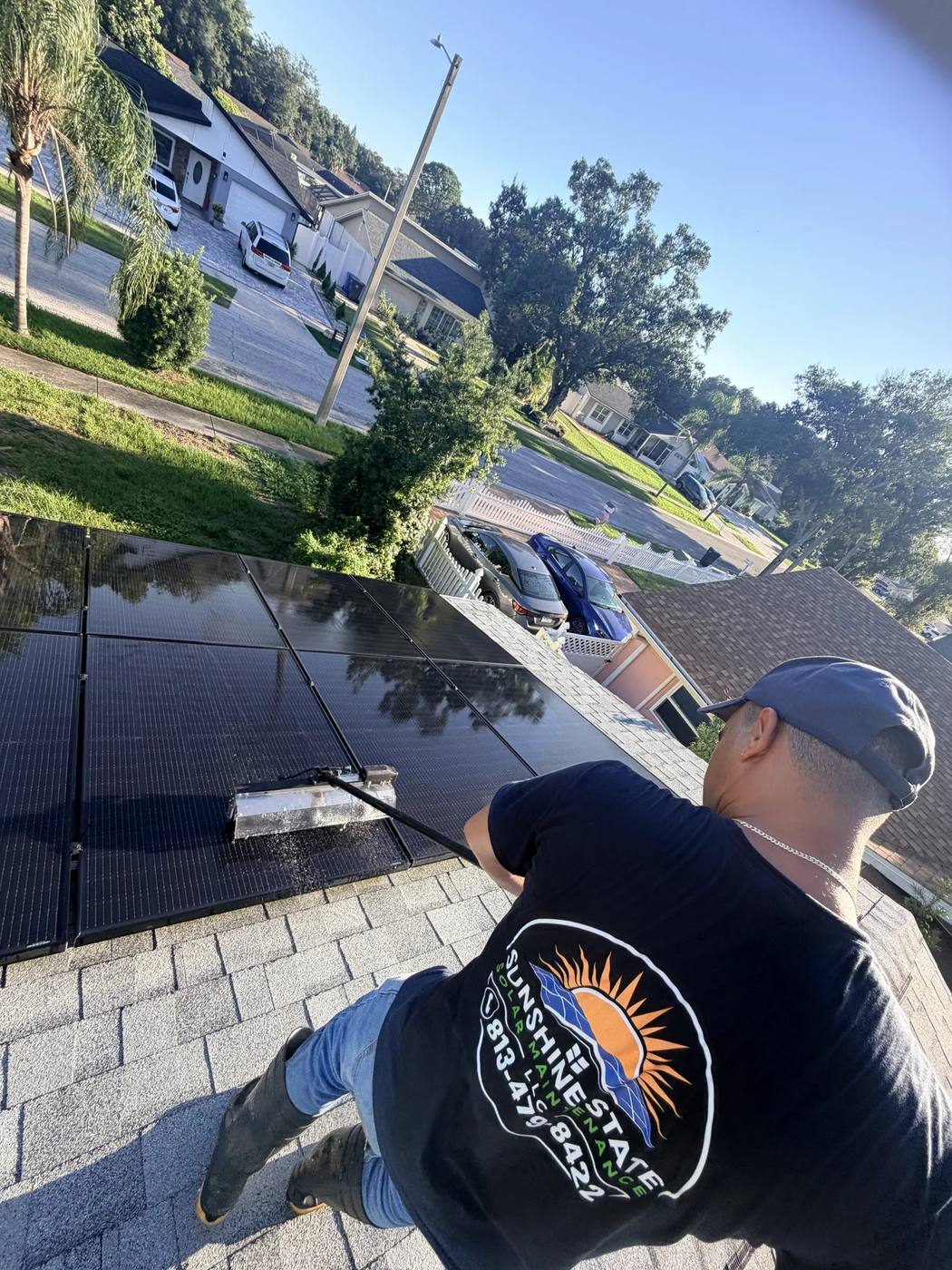 Sunshine State Solar Maintenance technician in a company shirt brushing a solar panel on a tile roof